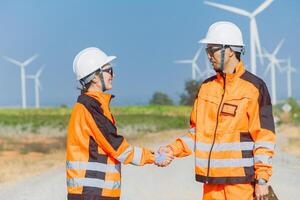 Two men in orange safety gear shaking hands in front of wind turbines photo