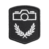 Black embroidered patch features white camera icon above two laurel branches, symbolizing photography achievement or membership. design is simple and elegant png