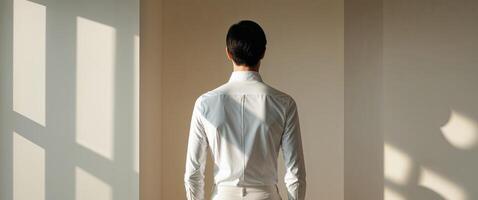Back view of person wearing white shirt with shadows on wall in soft lighting and neutral background photo
