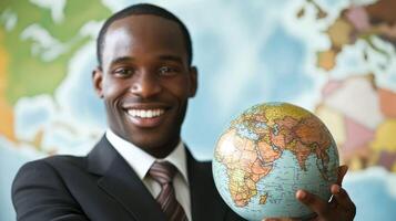 A smiling man in a suit holding a small globe in front of a world map. photo