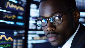 A man in a suit and glasses, looking at a computer screen with financial data in the background. photo