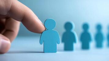 A hand is pointing at a blue wooden figure of a person, with a blurred row of similar figures in the background. photo