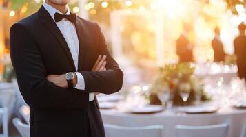 A man in a tuxedo standing in front of a table with a blurred background of a dining table and chairs. photo