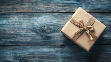 A rustic wooden table with a single gift wrapped in brown paper and tied with a string bow. photo