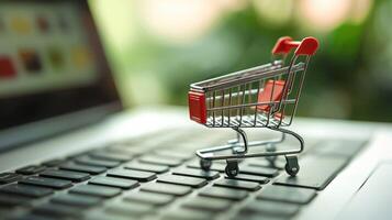 A miniature shopping cart with a red handle and black wheels, placed on a laptop keyboard with a blurred green background. photo