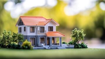 A miniature model of a house with a red roof and white walls, placed on a green lawn with trees in the background. photo