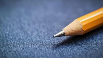 A yellow pencil with a sharpened tip lying on a dark blue textured surface. photo