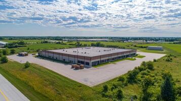 A large, empty industrial building with a flat roof, surrounded by green fields and a clear blue sky with white clouds. photo