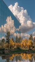Reflection of autumn trees and clouds on a glass building under a bright blue sky photo