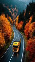 Vibrant autumn landscape with a yellow truck traveling along a winding road in the forest photo