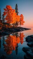 Autumn trees reflecting on calm water at sunset in a serene lakeside landscape photo