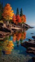 Vibrant autumn colors reflect on calm waters along a rocky lakeshore in the early morning light photo
