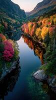 Vibrant autumn foliage reflects in tranquil river surrounded by mountains at sunset photo