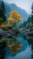 Bright yellow autumn tree reflecting in calm blue water surrounded by mountains and greenery photo