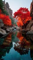 Autumn colors reflect in a serene river surrounded by vibrant red trees and rocky terrain in a tranquil landscape photo