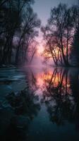 Misty sunrise over a tranquil river reflecting trees and vibrant colors in the early morning light photo