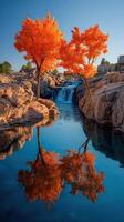 Vibrant autumn trees reflect in tranquil water near a waterfall under a clear blue sky photo