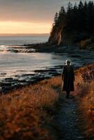 A man in a long coat walks down a path near the ocean photo