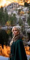 A beautiful blonde woman in a green cloak standing in front of a mountain photo