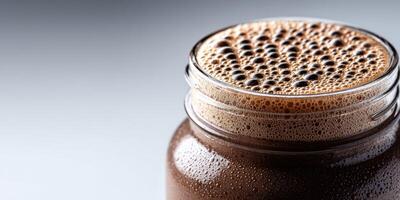 A thick, rich protein shake filled with bubbles sits in a clear glass jar photo
