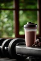 Protein shake on gym bench next to dumbbells in natural light photo
