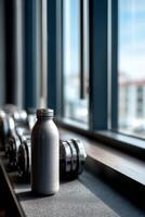 Protein shake resting beside dumbbells in a bright gym setting photo
