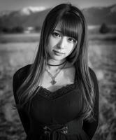 Young woman in black dress poses in rural setting with mountains photo