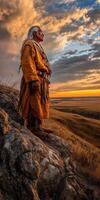 Native elder standing on rocky hilltop at sunset over plains photo