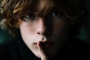 Young boy with curly hair making a shushing gesture indoors photo