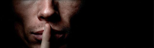 Man with finger to lips signaling for silence in dim lighting photo