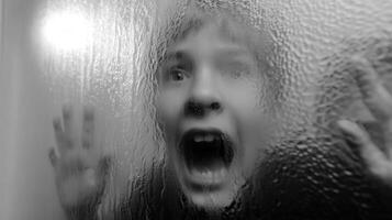 Child expressing fear behind frosted glass during evening hours photo