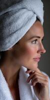Woman in a white towel reflecting calmly while looking out a window photo