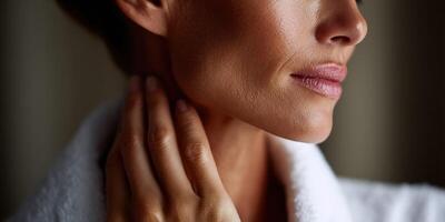 Woman in a bathrobe touching her neck in soft lighting at home photo