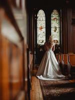 Bride stands gracefully before stained glass in elegant venue photo