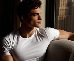 Model sitting thoughtfully by a window in a city setting during daylight photo