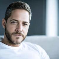 Man with beard relaxes indoors, natural light illuminating his expression photo