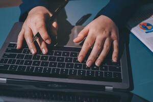 A person typing on a laptop with a pen in their hand photo