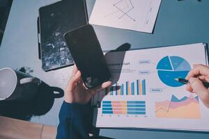 Businessman using a tablet and pen to write on a paper with graphs and charts photo