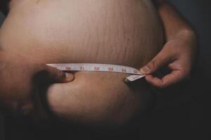 A person is holding a measuring tape around their stomach photo