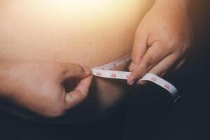 A person measuring their stomach with a tape measure photo