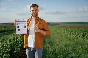 Graphs, and business analytics on document, notepad. Handsome man is on the agricultural field at daytime photo