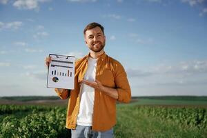 Graphs and, business analytics on document, notepad. Handsome man is on the agricultural field at daytime photo
