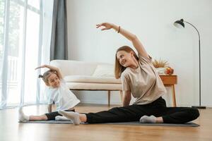 To the ,side, stretching. Young,, woman with little girl are doing yoga at home photo