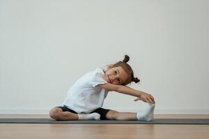 Stretching the leg. Cute little girl ,,,is sitting on the yoga mat and doing exercises photo