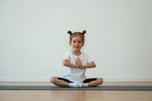 Cute little girl is sitting on the yoga mat, and doing exercises photo