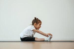 Side view, stretching. Cute ,,little girl is sitting on the yoga mat and doing exercises photo