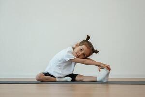 Stretching, the leg. Cute little girl is sitting on the yoga mat and doing exercises photo
