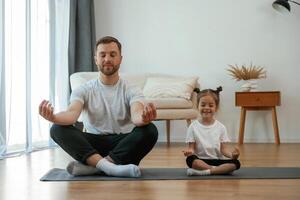 Lotus pose. Father with little daughter, are ,ing yoga at home photo