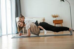 Lying down on the back of, mother. Young woman with little girl are doing yoga at home photo
