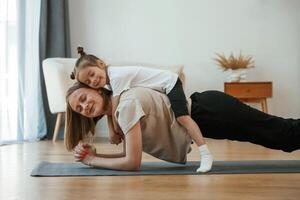 Lying down, on the back of mother. Young woman with little girl are doing yoga at home photo